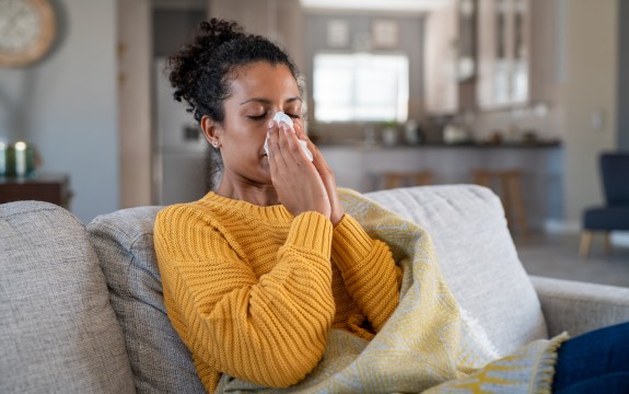African American woman wearing a yellow sweater blowing her nose