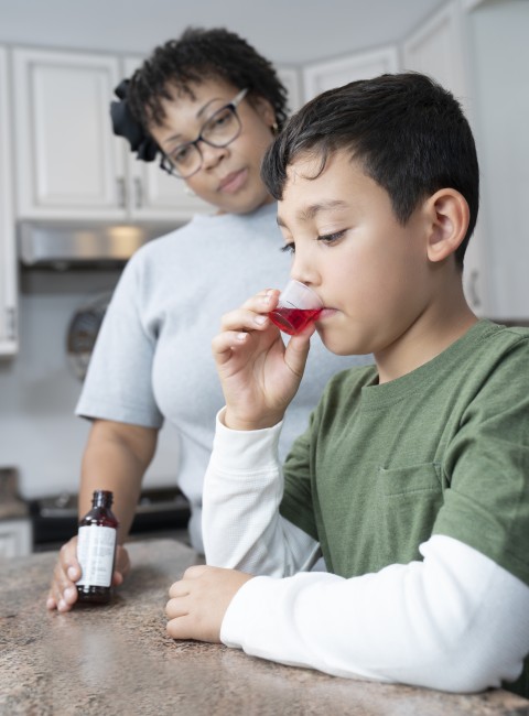African American/Black woman giving Hispanic/Latinx boy in green shirt liquid medicine