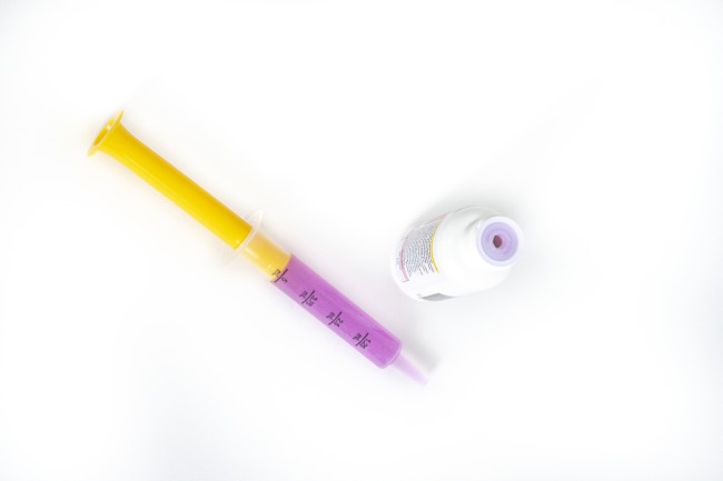 Dosing syringe with purple medicine and medicine bottle