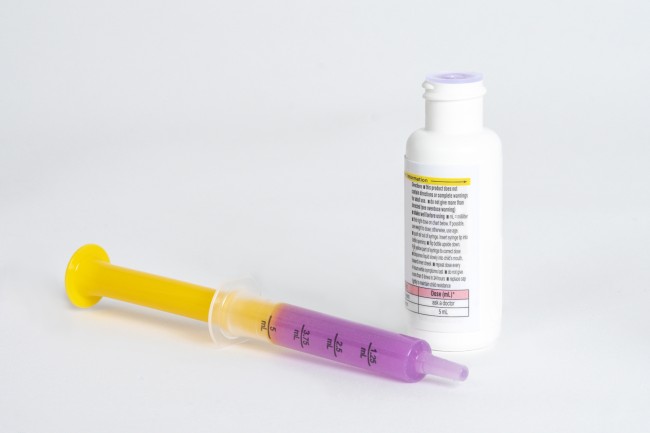 Dosing syringe with purple medicine and medicine bottle