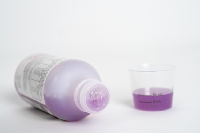Liquid medicine bottle on its side and dosing cup with medicine