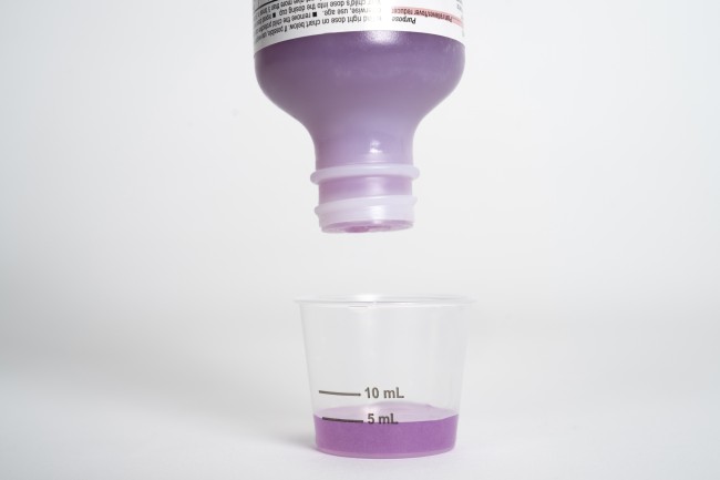 Purple liquid medicine being poured into dosing cup