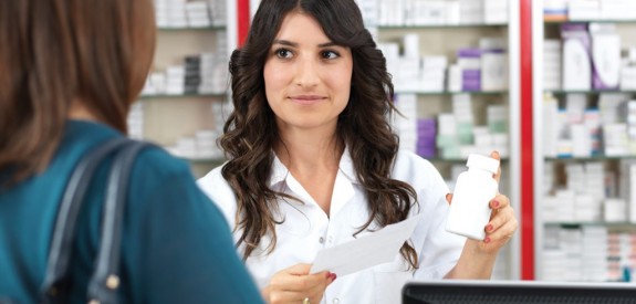 Pharmacist with long dark hair assisting customer in dark green shirt