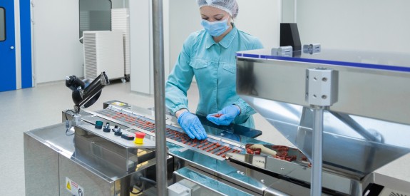 woman worker in protective clothing operating production of tablets in sterile environment