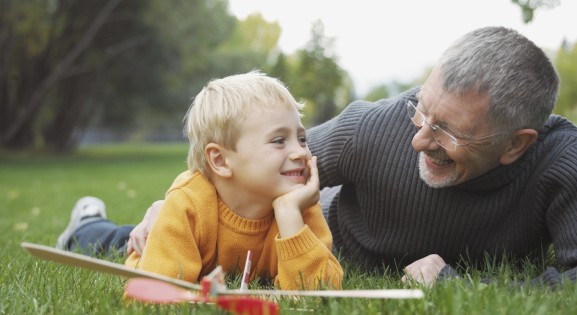 grandfather and grandchild laying on grass with a toy airplane