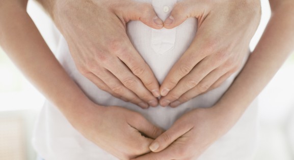 pregnant woman dressed in white with partner creating heart shape on her stomach