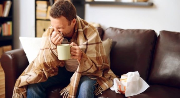 Man wrapped in a blanket blowing his nose.