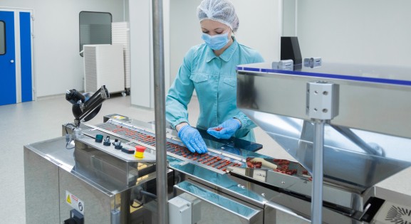 woman worker in protective clothing operating production of tablets in sterile environment