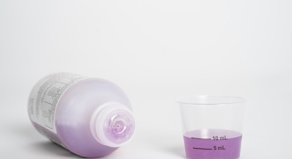 Liquid medicine bottle on its side and dosing cup with purple medicine