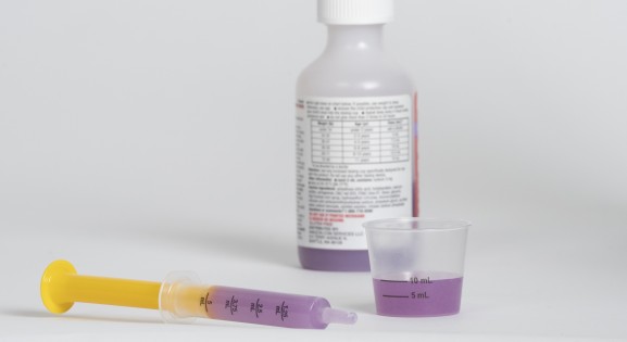 Medicine bottle, syringe, and dosing cup with purple liquid medicine