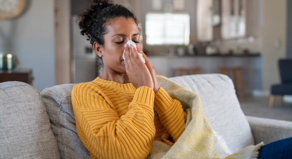 African American woman wearing a yellow sweater blowing her nose