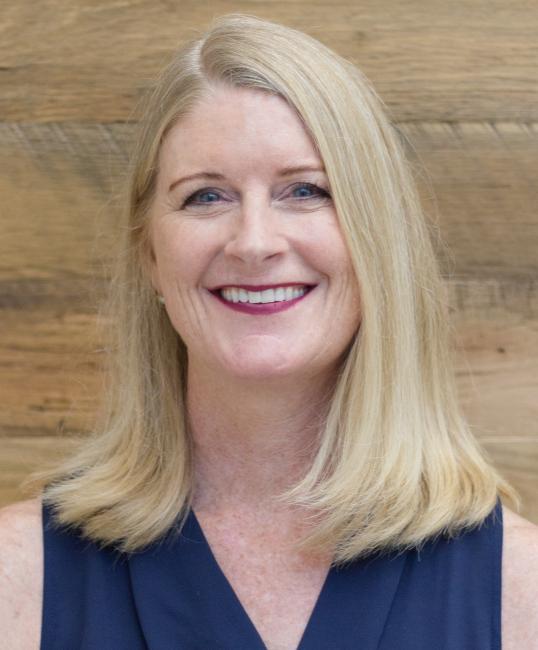 Beth Allgaier in front of a wood background with a dark blue blouse