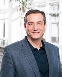 Headshot of Paul Gama with brightly lit background in a suit